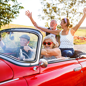 Es sitzen zwei Pärchen in einem roten Cabrio und haben Spaß