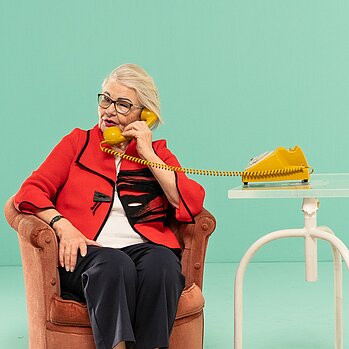 Ältere Frau sitzt in Sessel und telefoniert mit Schnurtelefon