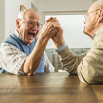 Zwei ältere Männer spielen Armdrücken und lachen sich an