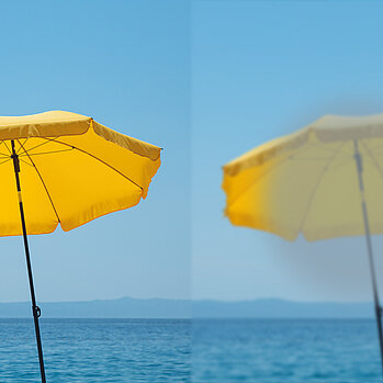 Gelber Sonnenschirm vor blauem Meer + Himmel, einmal scharf und einmal unscharf
