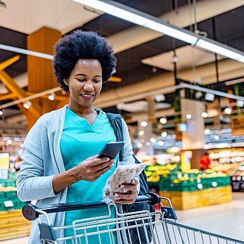 Frau im Supermarkt schaut auf ihr Handy