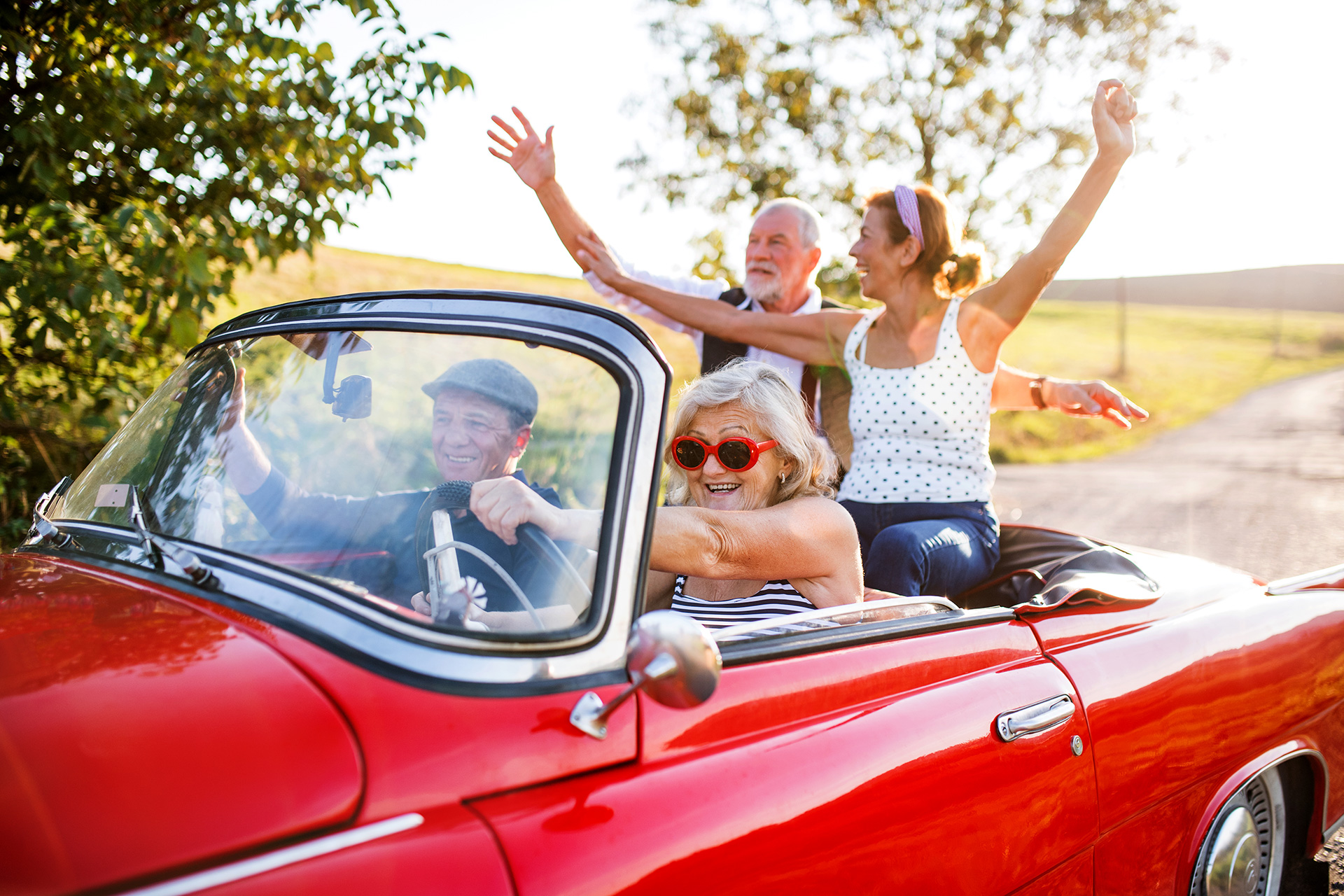 Es sitzen zwei Pärchen in einem roten Cabrio und haben Spaß